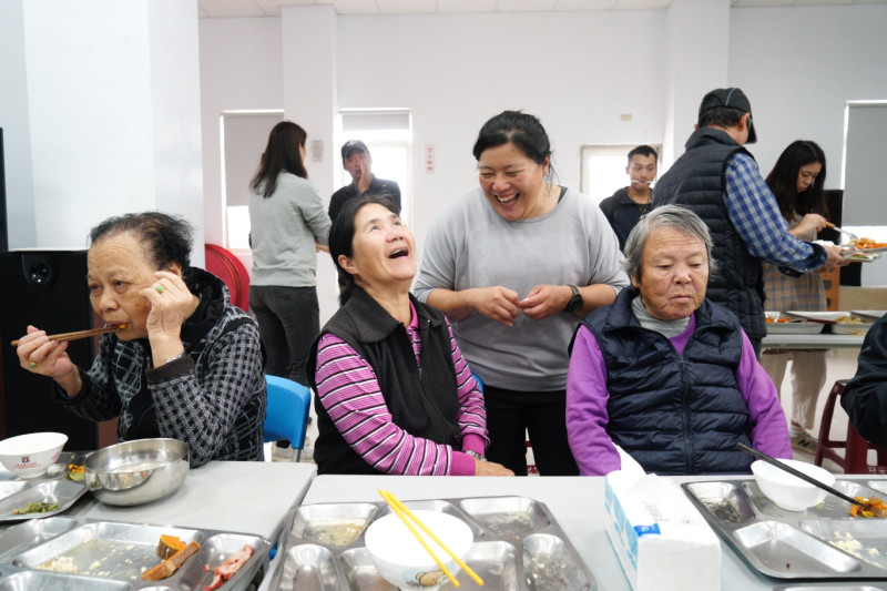 東莒社區發展協會舉辦的老人共餐活動，在「關島」期間如常進行，為老人家準備餐食的小葵（右二）和老人家們愉快聊天。   圖：張良一/攝
