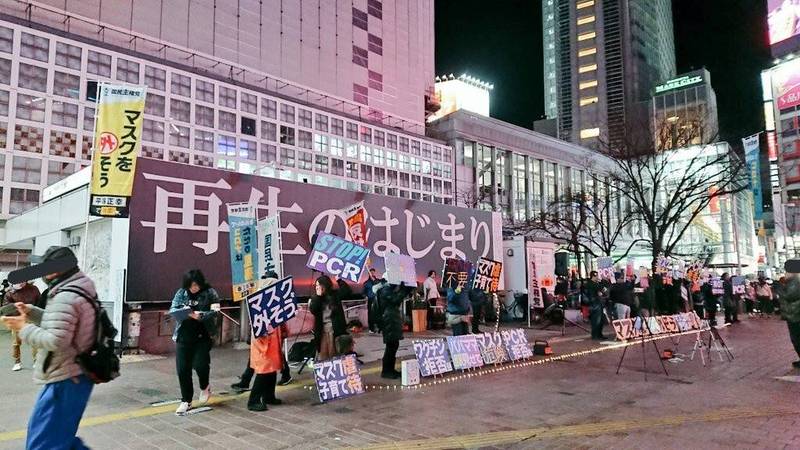 日本武漢肺炎疫情快速升溫，近日網路流傳一張照片，一群人在東京街頭舉標語，呼籲路人「別戴口罩，露出笑容」，並稱武漢肺炎是「為了淨化世界，讓世界重生」。   圖：翻攝自推特