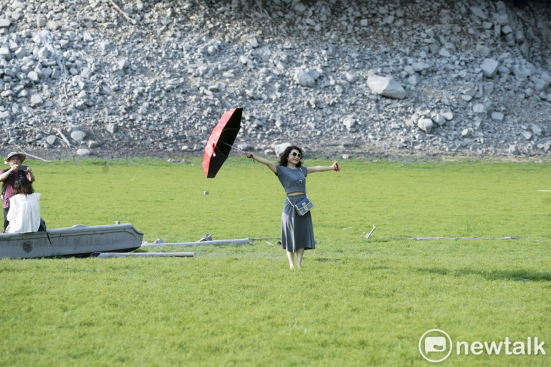 一位遊客撐傘並張開雙手在「日月潭大草原」拍紀念照。   圖：張良一/攝