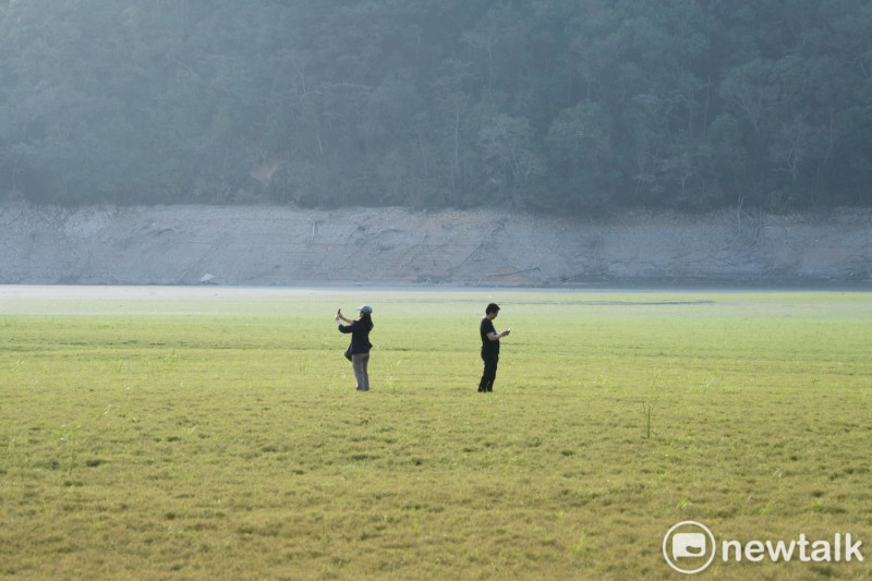 兩位遊客在「日月潭大草原」拍攝水庫乾涸奇景。   圖：張良一/攝