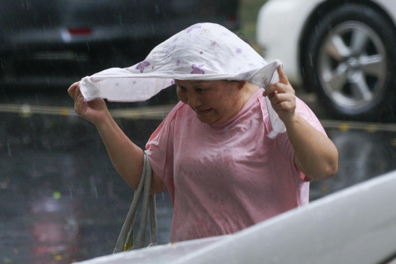 台北市區上午下了一長大雨，一位民眾用衣服遮雨。   圖：張良一/攝