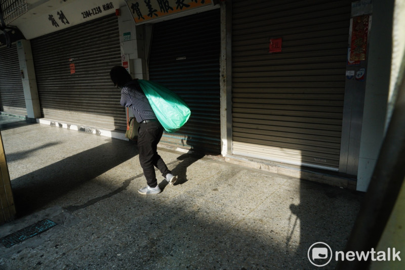 一位民眾扛著綠色大包袱走過沒有開店營業的成衣街。   圖：張良一/攝