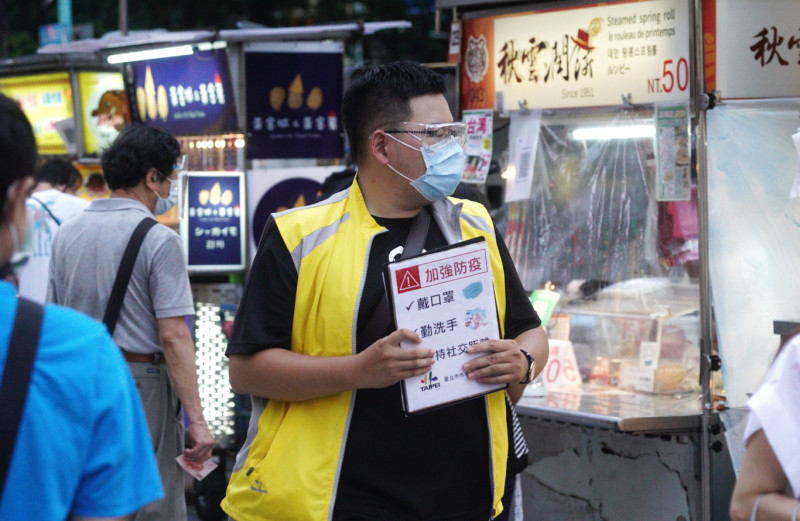 台北市政府市場處的一位人員在寧夏夜市宣導市民做好個人防疫措施。   圖：張良一/攝