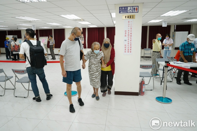 一位老黨員在家人和外籍移工的扶持下，前往投票所，並順利完成投票。   圖：張良一/攝