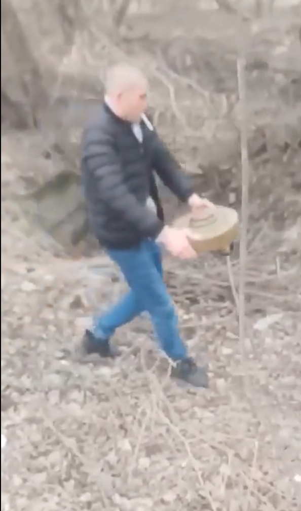 一名烏克蘭男子一邊叼菸一邊將地雷移至樹林中。   圖/截自The New Voice of Ukraine 推特帳號