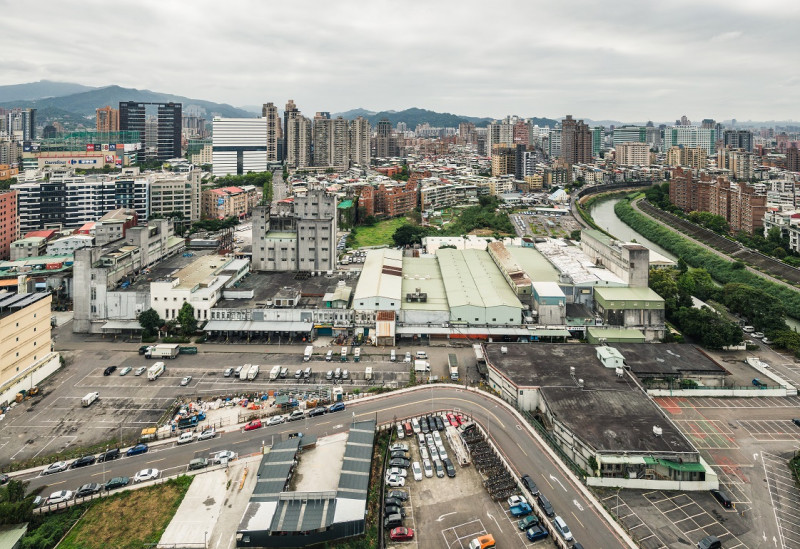 新店榮工單元2位於新店區東北隅，北側以景美溪為界與台北市文山區相鄰，計畫區內現況主要為正大尼龍工業之倉儲及辦公使用，而西側多為老舊低矮住宅，東側主要為停車場使用，南側為裕隆、宏達電等企業總部及大型賣場如家樂福等。   圖：新北市城鄉局提供