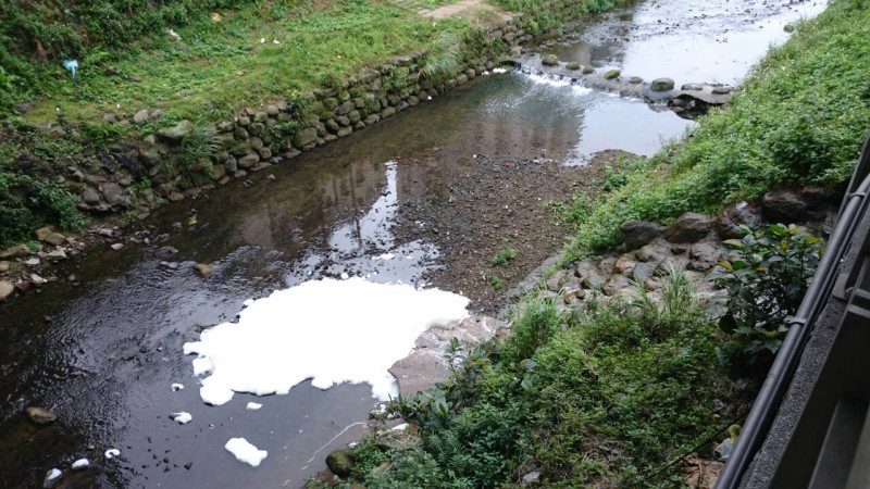 汐止遠雄購物中心違法排放污水，造成了附近康誥坑水面上積了厚厚一層白色泡沫，綿延大約100公尺。   圖：翻攝自新北市環保局官網