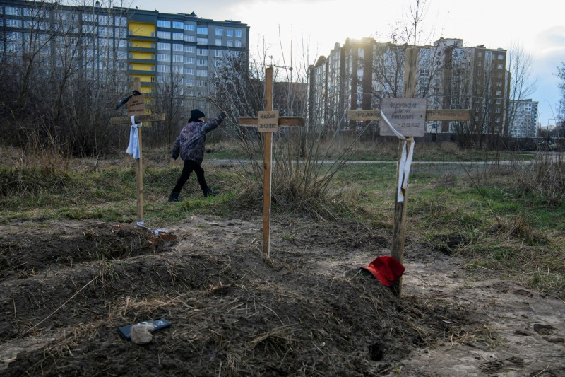 在烏克蘭基輔地區的布查（Bucha），一名男孩帶著平民的屍體走過墳墓，當地居民表示，這些平民被俄軍殺害，而中間十字架上的銘文寫著「未知」。   圖：達志影像/路透社
