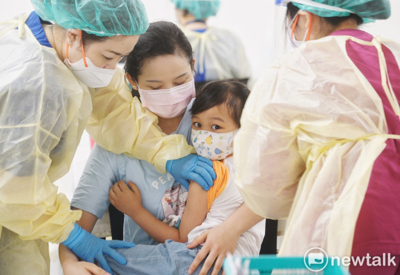 一位媽媽將她的女兒緊緊的摟在懷裡，一旁的護理人員也幫忙按住她的手臂，以接種新冠肺炎疫苗。   圖：張良一/攝