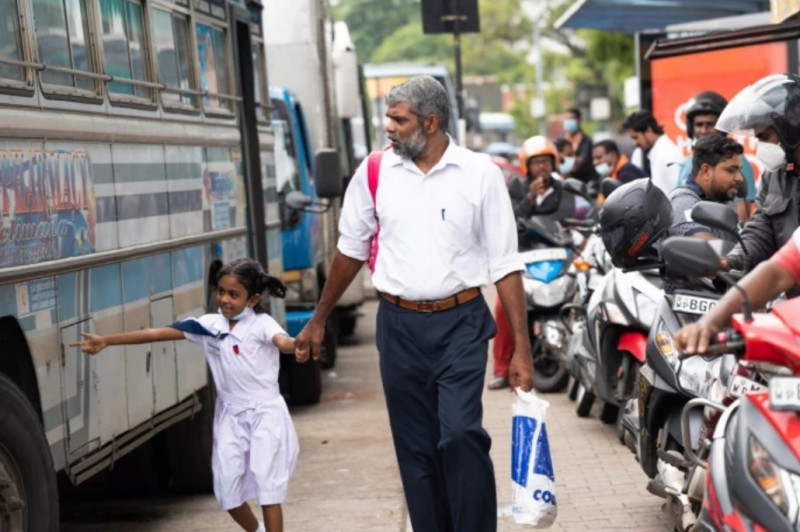 2022年6月9日，一名父親帶著剛放學的女兒走在排隊等燃油的公共汽車與摩托車之間。   圖：翻攝自新華社