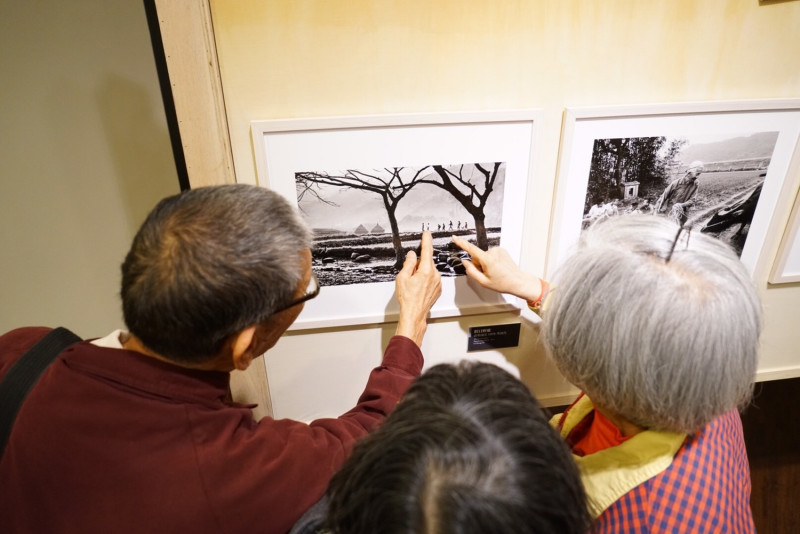 印象台三線攝影展的參展攝影家李湞吉（手指照片）的，向照片中人的本尊，介紹當時攝影的故事。   圖：台灣水/黃裕順提供