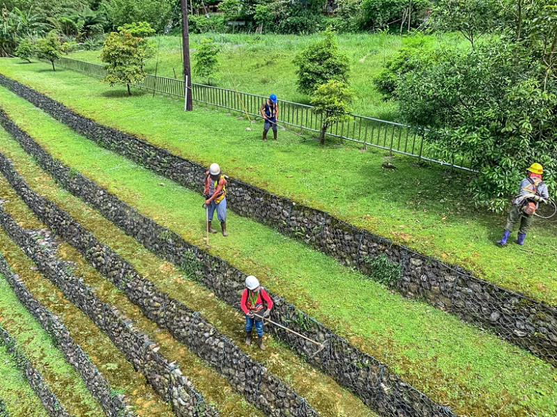 工作人員揹著除草機站在層層堆疊的石籠護岸執行除草工作。   圖：新北市水利局提供