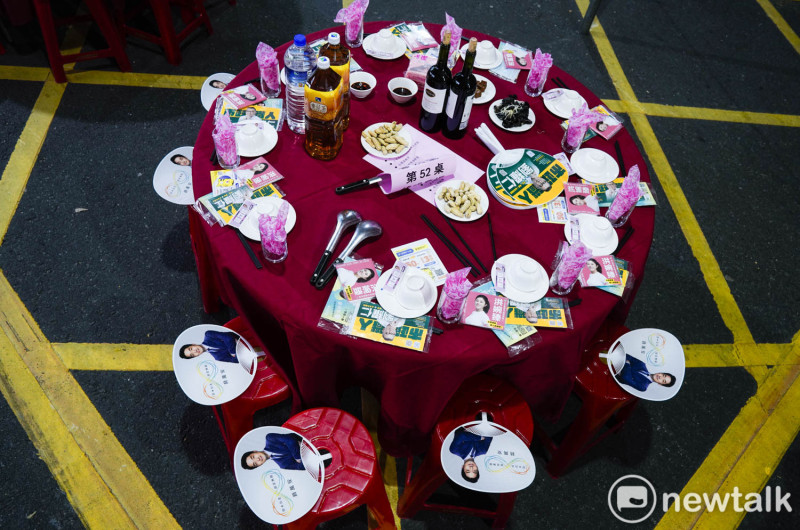 台北環南市場自治會在市場外封街舉辦聯誼餐會，寫著候選人名字的口罩、面紙、扇子塞爆了桌子和椅子。   圖：張良一/攝