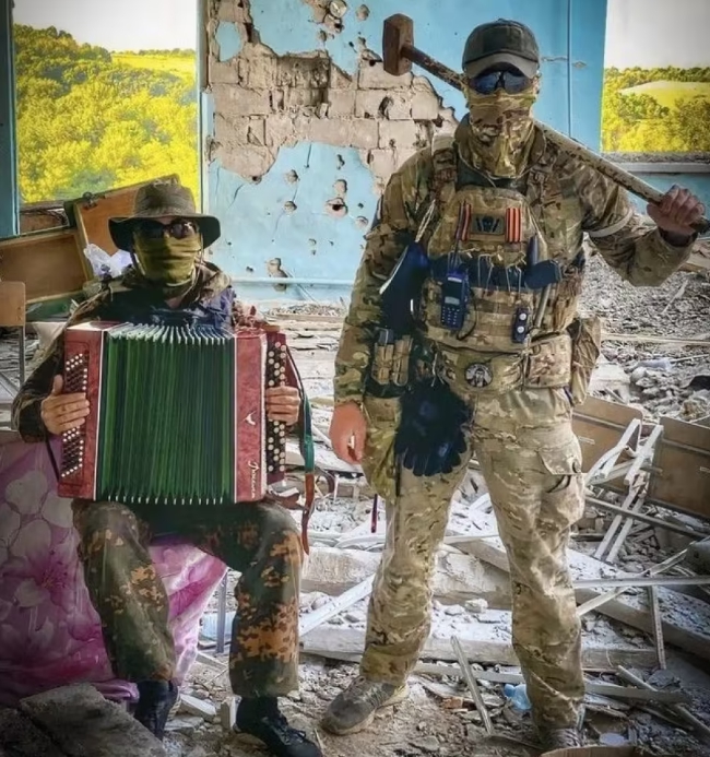 俄軍瓦格納集團傭兵公開展示錘刑，還有人拉手風琴在現場伴奏「助興」。   圖 : 翻攝自陸媒《迷彩虎》