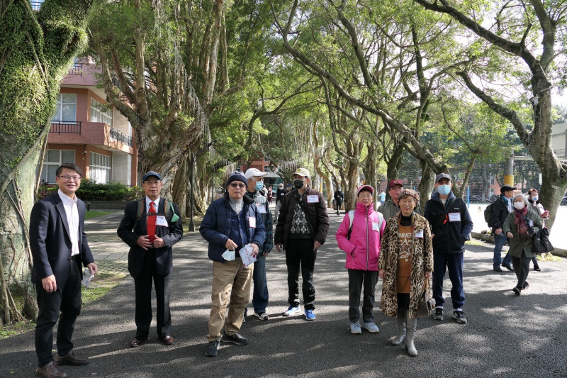 醒吾科大副校長鍾志明（左）帶領畢業50年校友漫步林蔭大道，回想當年的小樹如今已茁壯成大樹，校友們滿臉甜蜜笑容。   圖：醒吾科大提供