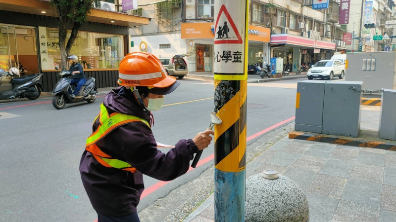 清潔隊撕除小廣告後刮除殘留的黏貼痕跡。   圖：新北市環保局提供