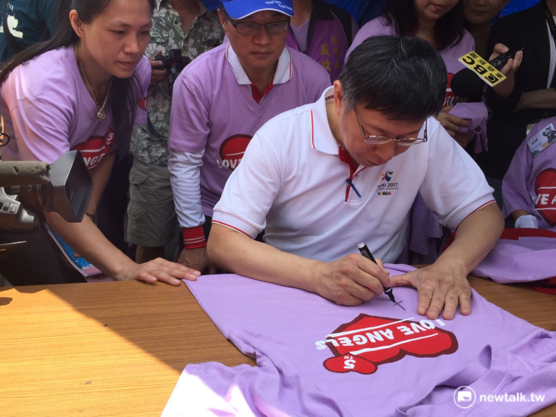 柯文哲7日出席「第五屆愛天使樂活園遊會」，為活動敲鑼開場，他並在活動T恤上簽名。   圖：林人芳／攝