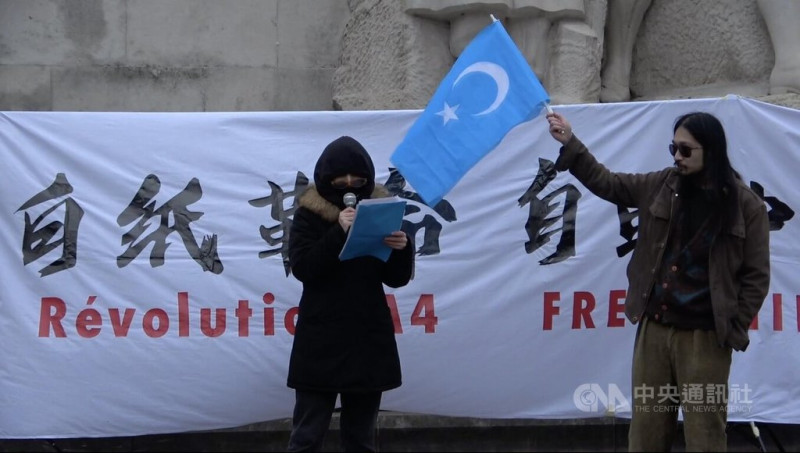 法國「反賊」社群的帶領者蔣不在2018年抵法後經常組織民主活動，社群從寥寥數人到如今約200人，經投票取名為「自由廣場」。圖為2022年12月3日「自由廣場」主辦的巴黎白紙革命運動，蔣不（右）為維吾爾族發言民眾高舉東突厥斯坦旗幟。   圖/中央社