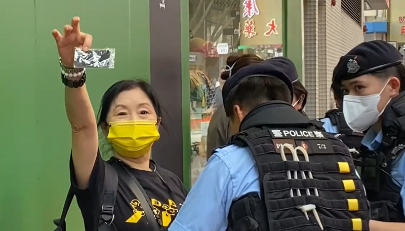有一位香港女士，被多名警察搜查時，看到圍觀拍攝者，淡定從包包裡拿出寫著「良知」的卡片。   圖：翻攝自彥子lanni推特