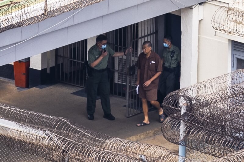 黎智英在香港赤柱監獄內穿著短褲和涼鞋，手中握著一本書在兩名獄警陪伴下散步。   圖 : 達志影像/美聯社
