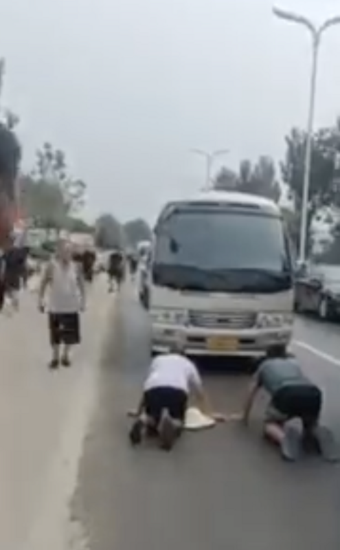 涿州災民跪在官員乘坐的巴士前抗議，希望能當面向官員成情。網友根據車輛分析，推測該車輛為河北省長座車。   圖：翻攝自Ｘ／@fangshimin