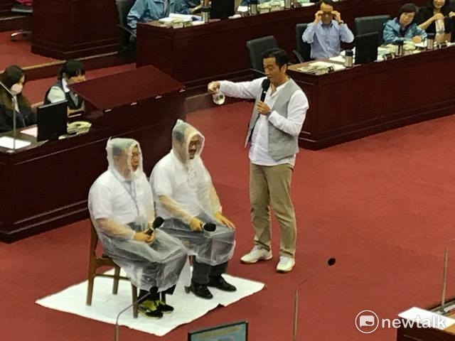 市議員李傅中武朝著鍾永豐噴水，體驗只穿雨衣未戴傘帽的情境。   周煊惠／攝