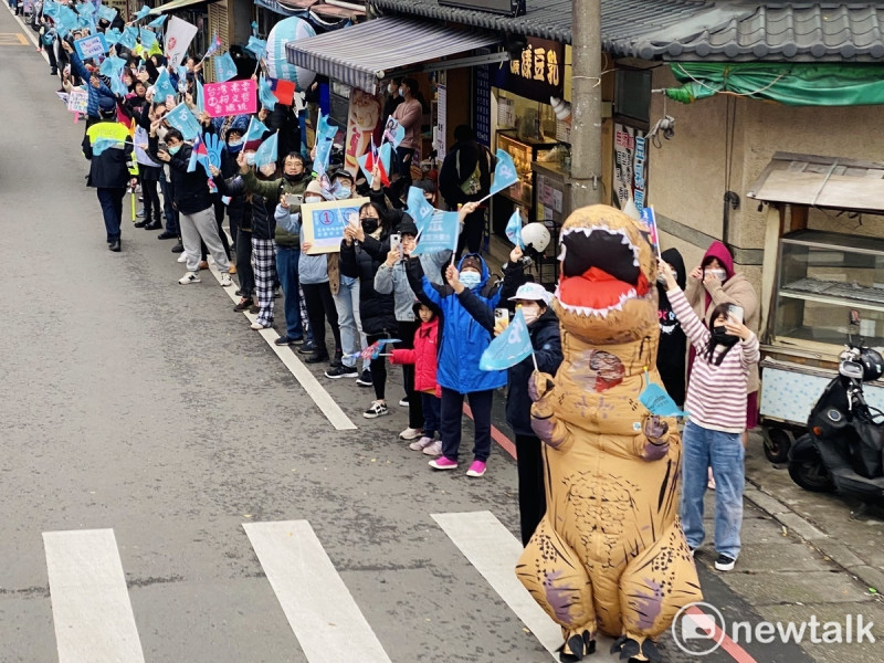 民眾黨總統候選人柯文哲支持者站在路邊揮舞民眾黨旗幟,還有民眾穿恐龍裝揮旗幟表達支持。 圖:周煊惠 / 攝