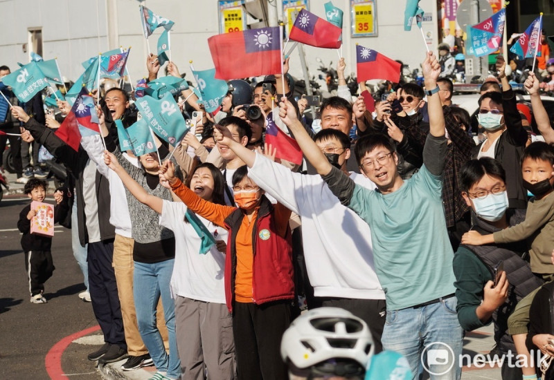 年輕的民眾黨支持者站在柯文哲掃街車隊行經的路旁，高舉旗幟為柯加油打氣。   圖：張良一/攝