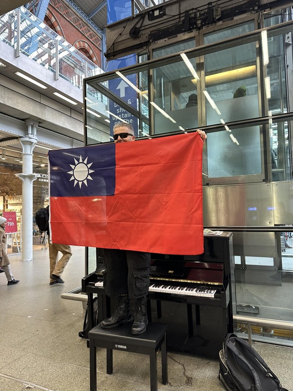 卡瓦納站在鋼琴椅上，手裡拿著一面中華民國的青天白日滿地紅國旗。   圖：翻攝卡瓦納臉書