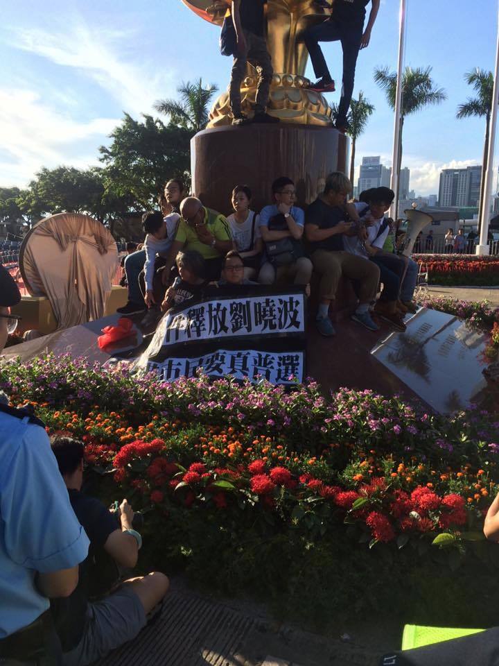 香港眾志約26名成員是在28日下午到金紫荊像，掛上印有「無條件釋放劉曉波，香港市民要真普選」等的黑布標語，一度以鐵鏈纏腰，意圖留守抗議。   圖:翻攝自香港眾志臉書