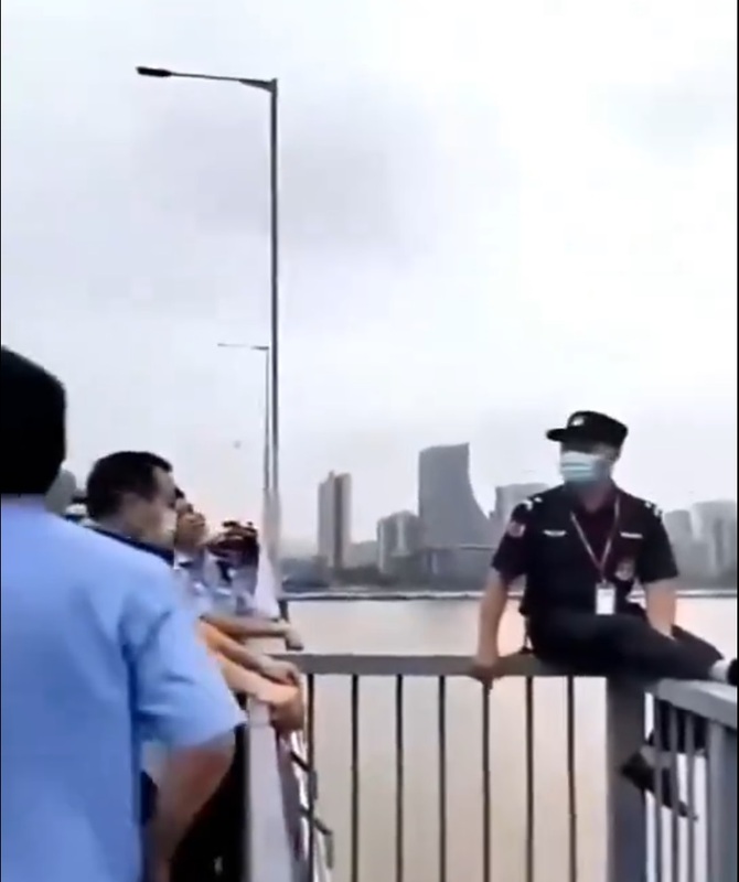 一名中國公安坐在橋邊的圍欄上，想要跳江，旁邊的警察不斷勸阻。   圖：翻攝自 Petrichor X（前推特）帳號
