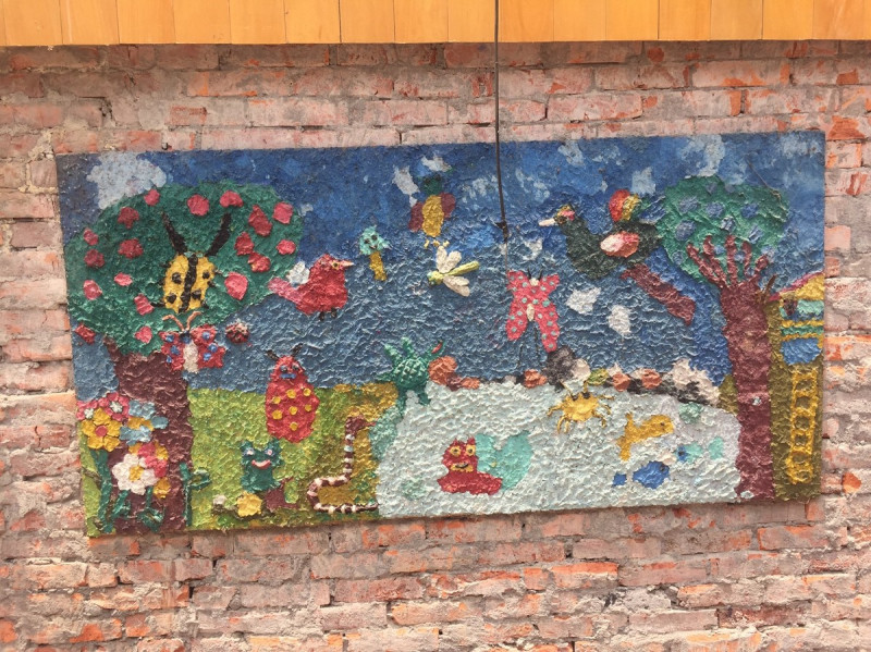 色彩飽滿的兒童創作，掛置於斑駁的紅磚牆上，展現樸質的氛圍與生命力。   圖：桃園市政府提供