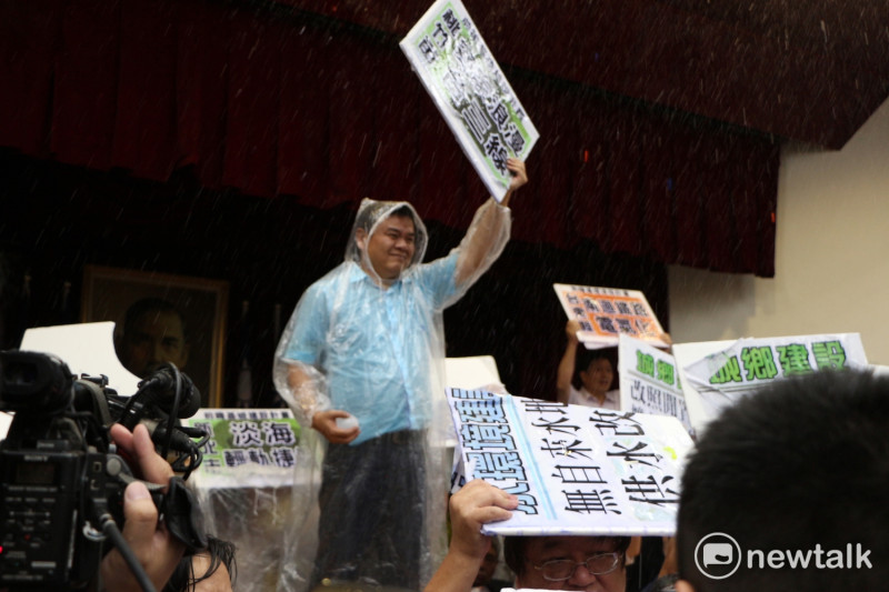 民進黨立委莊瑞雄，穿著雨衣，站在台上高舉抗議的板子，抵擋藍委們的攻擊。   圖：廖品瑄/攝
