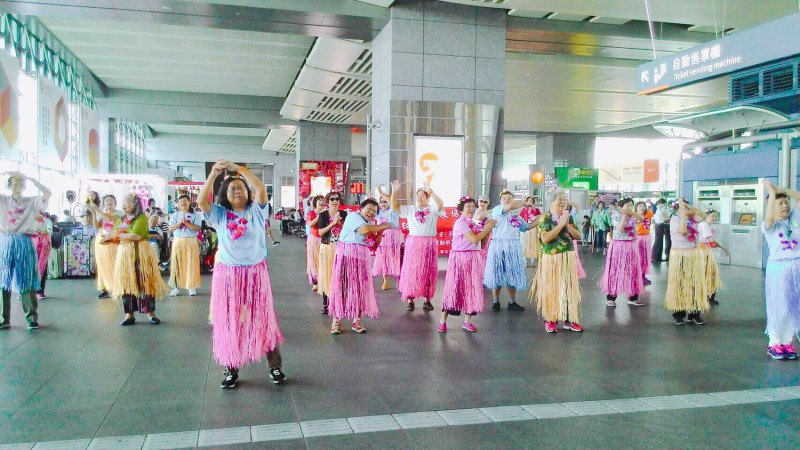今日(25)在高鐵台中站，大雅區文雅社區發展協會長輩們穿戴自製草裙與花圈，在老歌的伴隨下進行一段舞蹈的演出。   圖：台中市社會局提供