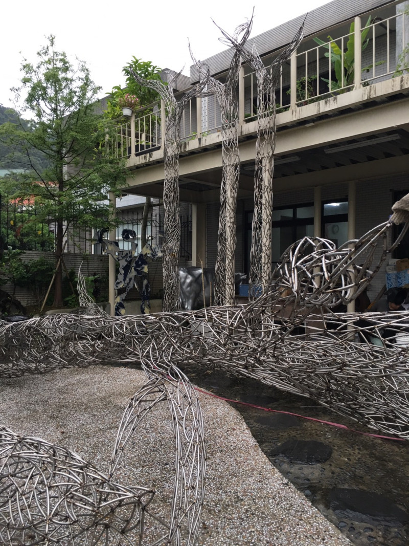 藝術家劉柏村挑戰以不鏽鋼材質製作白千層樹，與真實存在的白千層林道，相映成趣。   圖：桃園市文化局提供