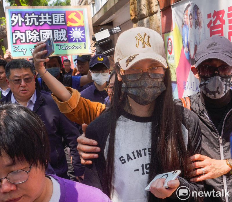 記者會後，警方護送亞亞離去，有人在亞亞背後高舉『外抗共匪 內除國賊』標語。   圖：張良一/攝