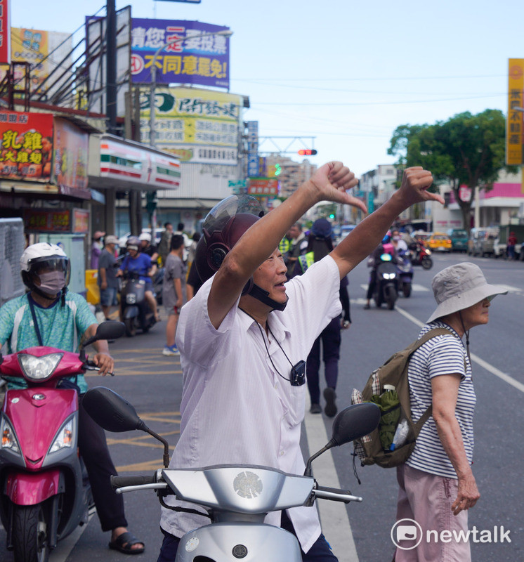 一位市民在花蓮吉安鄉黃昏市場前,對著參與護國大遶境的罷團志工比倒讚。在他的背後有一面巨幅的「請您ㄧ我一定要投不同意罷免」的廣告看板。 圖:張良一/攝