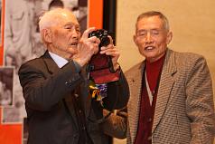 客委會客家文化發展中心8日舉辦「客庄生活影像故事」新書發表會，應邀出席高齡97歲的攝影家張阿祥（左）拿起相機記錄下發表會過程。圖片來源:中央社   