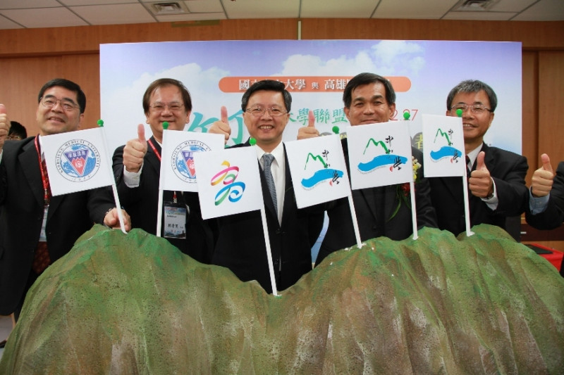 中山、高醫兩大學合作簽署「攻頂大學聯盟」，由高雄市副市長陳啟昱見証，三方並在象徵高雄的一座假山的山頭插下高雄市旗和兩校校旗。圖片來源：高雄市政府   