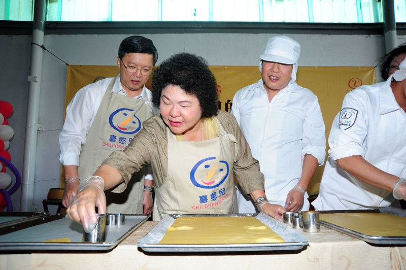 高雄市長陳菊一時技癢，捲起袖子與喜憨兒學員一同製作憨兒臉餅乾。圖片來源：高雄市政府提供。   