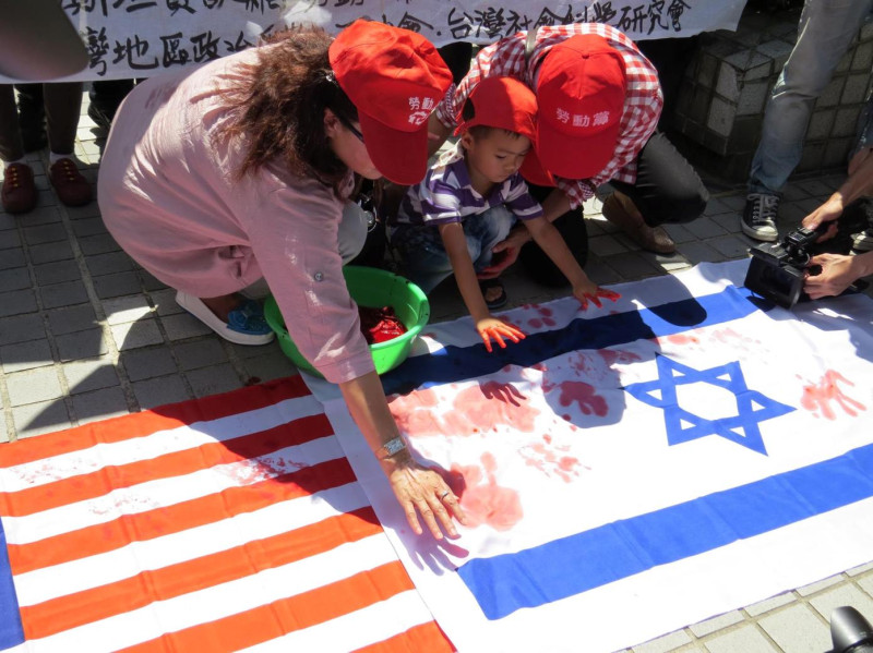 在場人士28日以手掌沾染紅色顏料後印蓋在美國及以色列國旗上，對兩國的血腥軍事行動表達抗議。 圖：蘇恆萱/攝   