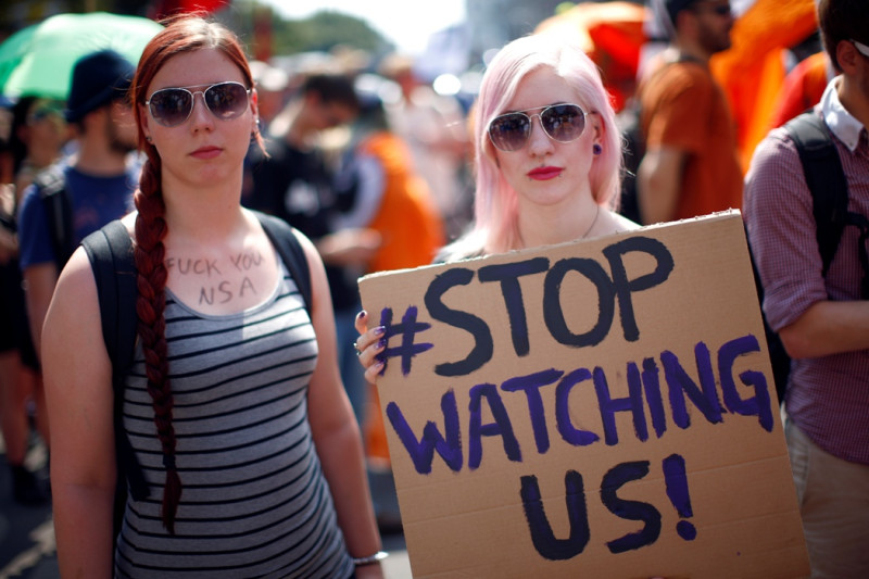 德國柏林27日舉行示威遊行，抗議美國國安局(NSA)透過「稜鏡」(PRISM)等計畫監控全世界，並展現對揭密者史諾登(Edward Snowden)和曼寧(Bradley Manning)等人的團結與支持。圖中這兩位年輕的女性，一名手上舉著標語：「停止監控我們！」另一名在身上胸口寫上：「Fxxx去你的NSA」。圖片來源：達志影像/路透社。   