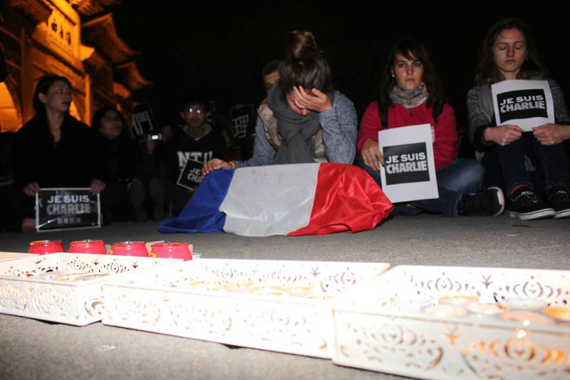 一名法國女子拿著法國國旗，坐在蠟燭前方，時而低頭、時而掩面，神情相當嚴肅。圖2之2：林雨佑/攝   