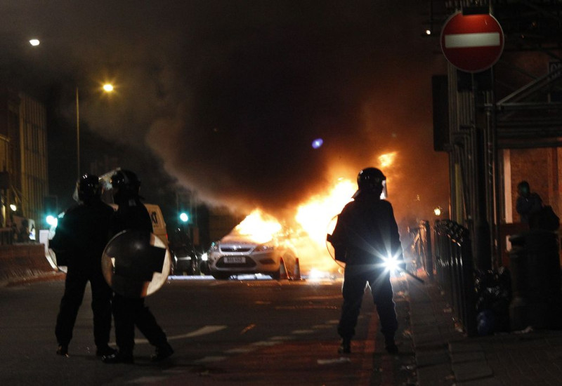 倫敦北部托登罕6日爆發嚴重警民衝突，圖為防暴警察在遭焚毀的警車前警戒。圖片來源：達志影像/路透社。   