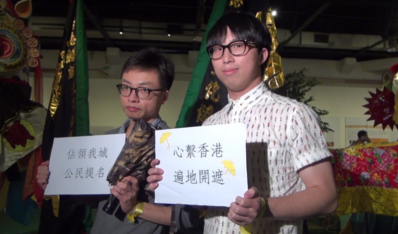 在今(17)天「香港週」的開幕式上，有2名港籍工作人員撐起大傘、手舉標語，隔海聲援香港佔中運動。圖：邱珮文/攝   