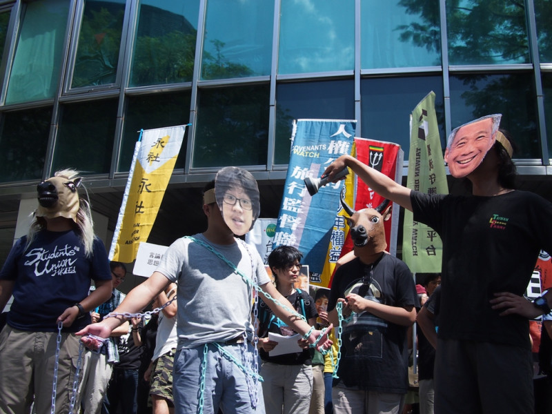 公民團體在現場演出帶著面具的李顯龍(右)，手拿著燈光照射被鐵鍊囚禁的Amos Yee(左)，以及牛頭馬面的行動劇，表達對新加坡政府作為的抗議。圖:何星瑩/攝。   