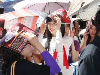 台北市氣溫回升，民眾在百貨公司外排隊進場血拼，因曝曬在陽光下，有人撐起陽傘遮陽，有些人則用百貨公司的廣告傳單遮蔽。提供：中央社   