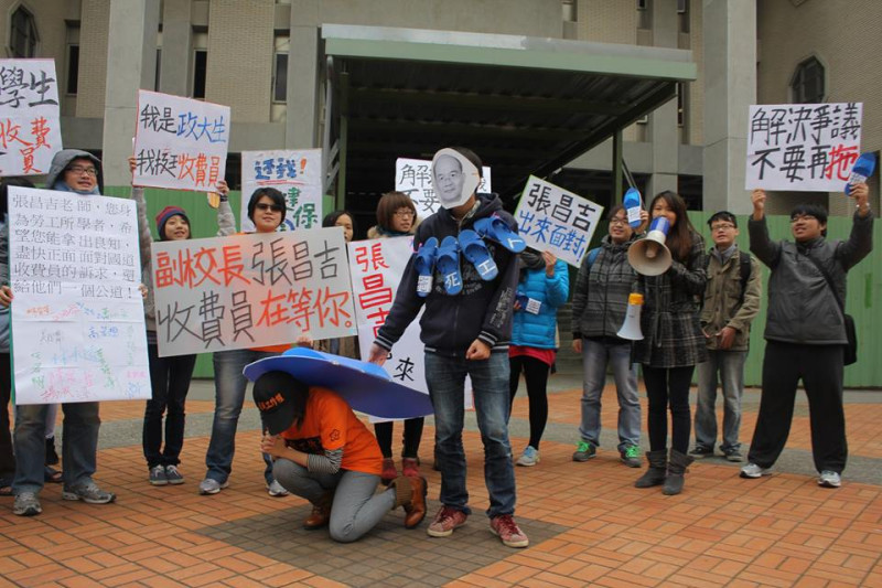 政大學生在行政大樓前演出行動劇，扮演副校長張昌吉的學生以象徵「拖」的大拖鞋，壓在收費員身上。圖：林雨佑/攝   