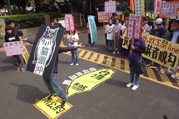 外勞團體高喊「本勞外勞，同工同酬」、「外勞越便宜，本勞越悲哀」等口號，並在行政院前演出行動劇，形容「貓頭冲」的政策是讓外勞人在台灣，卻要假裝自己不在台灣，進而領取低於基本工資的薪水。圖片：楊宗興/攝   