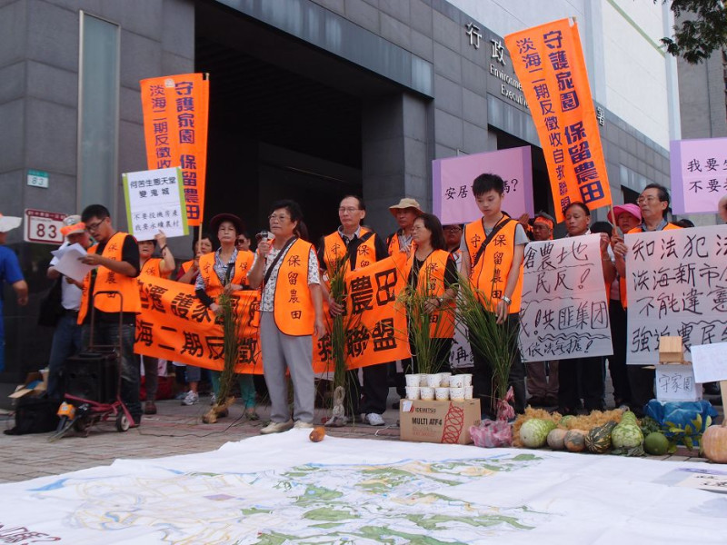 淡海二期反徵收自救會今天上午在環保署前舉行記者會，當地居民林洪清子控訴僅剩的農舍又要被徵收。自救會並在地上擺放當地盛產的蔬果和開發地圖。圖：陳柔伊/攝   